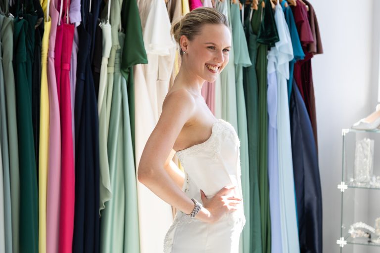 Bride in a strapless gown beside a rail of coloured bridesmaid dresses