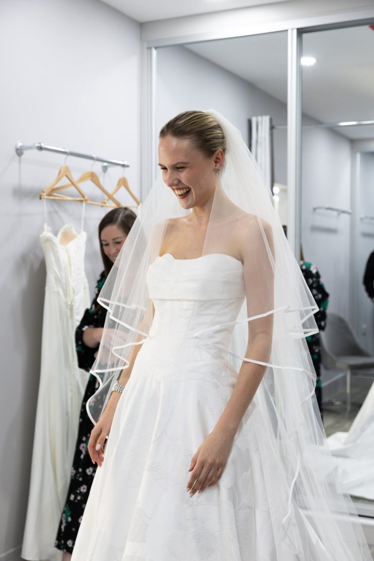 Smiling bride trying on a strapless gown and veil at VBB